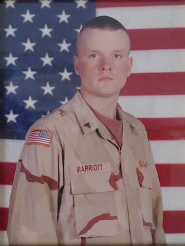 A soldier in uniform standing next to an american flag.