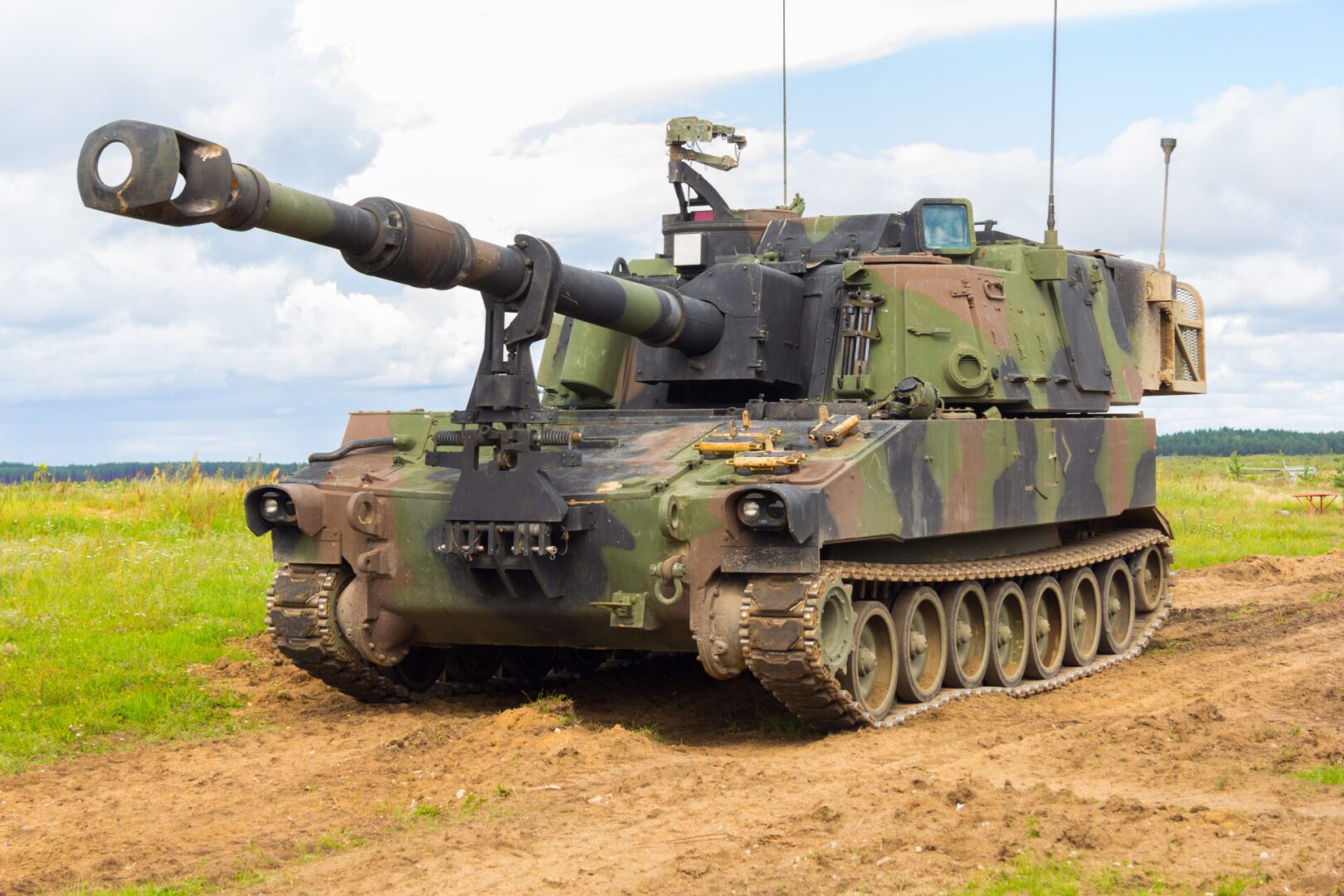 A military tank is driving down the dirt road.