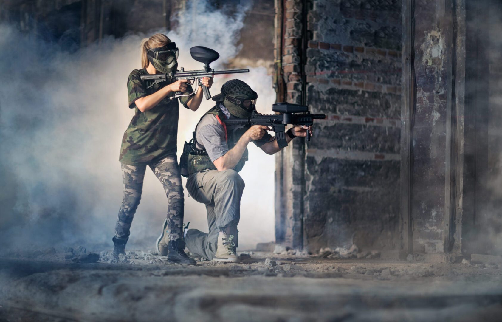 Two people in full gear are playing paintball.