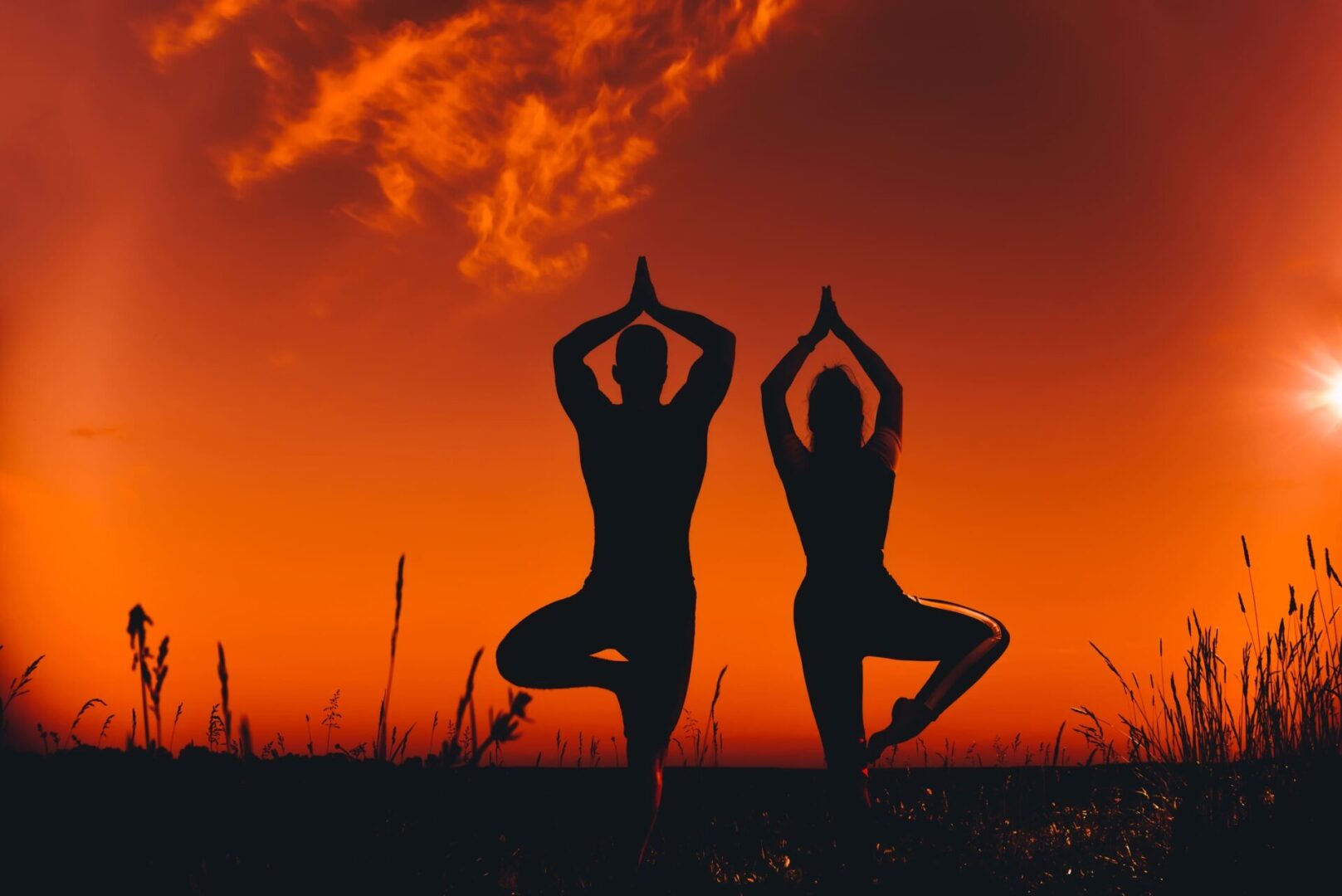 Two people are doing yoga in the sunset.