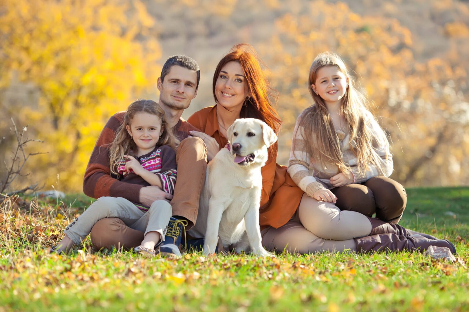 A family sitting on the grass with their dog.