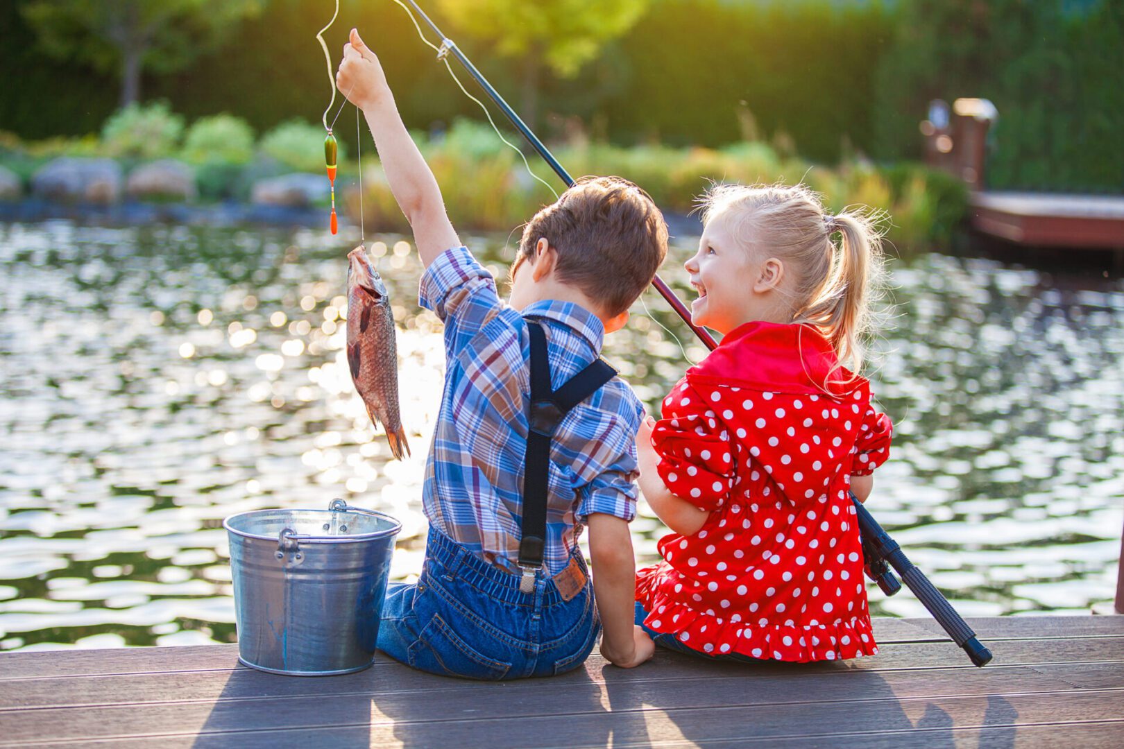 A boy and girl sitting on the dock holding fishing rods.