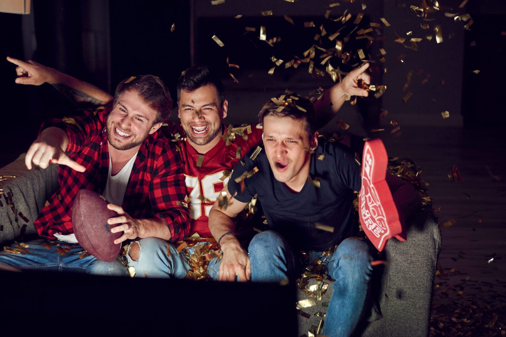 Three men sitting on a couch with beer and confetti flying around them.