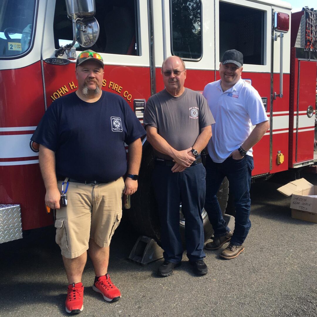 Three men standing in front of a fire truck.
