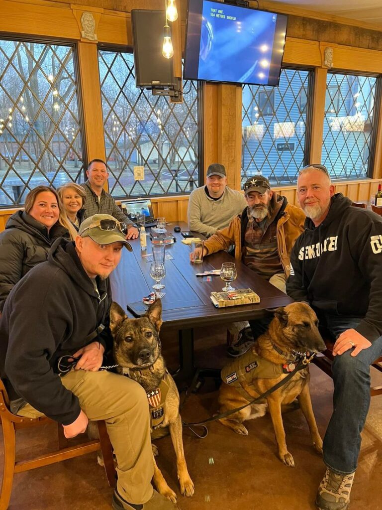 A group of people and two dogs sitting at a table.
