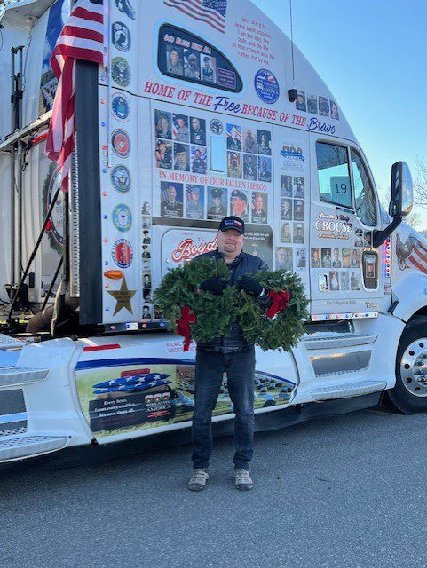 A man standing in front of a semi truck with wreaths on it.