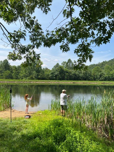 Two people fishing in a pond with reeds in the background.