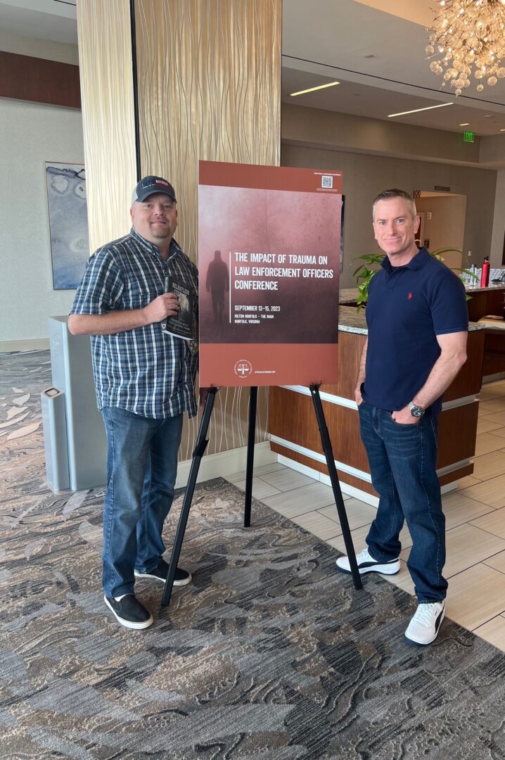 Two men standing next to a sign in front of a hotel lobby.