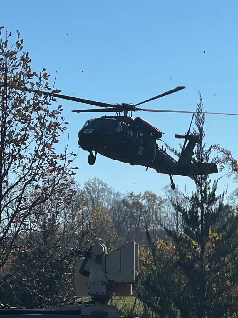 A black helicopter flies over a tree.