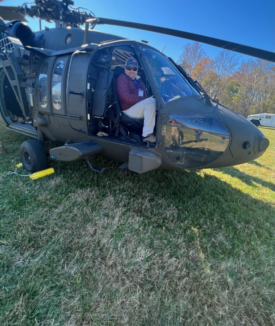 A man sits in the cockpit of a black helicopter.