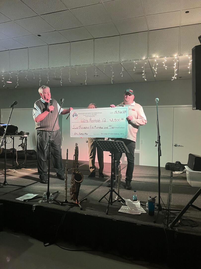 Two men standing in front of a microphone and holding a check.
