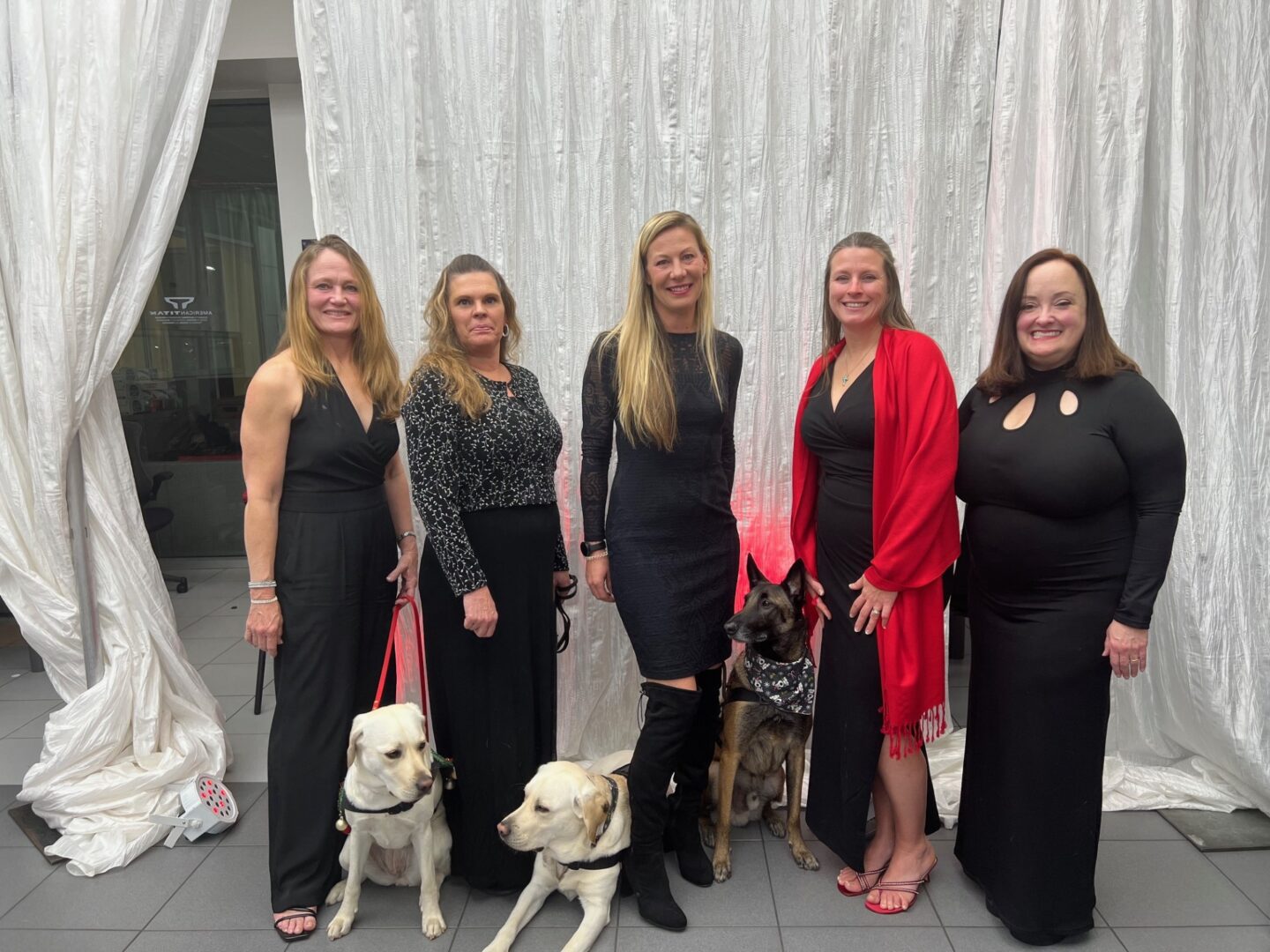 A group of women in black dresses posing with their dogs.