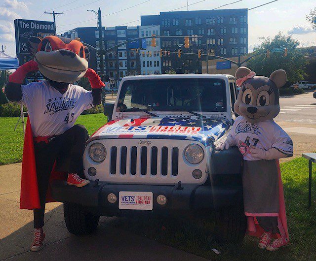 Mascots pose with jeep and american flag.