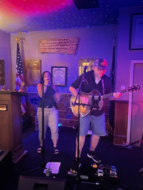 Two musicians perform on stage with guitar.